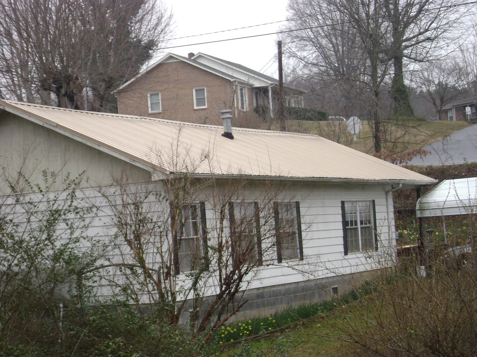 Tan metal roof on a white sided house set into a hillside — Commercial Roofing by Roofing Brothers in Kent